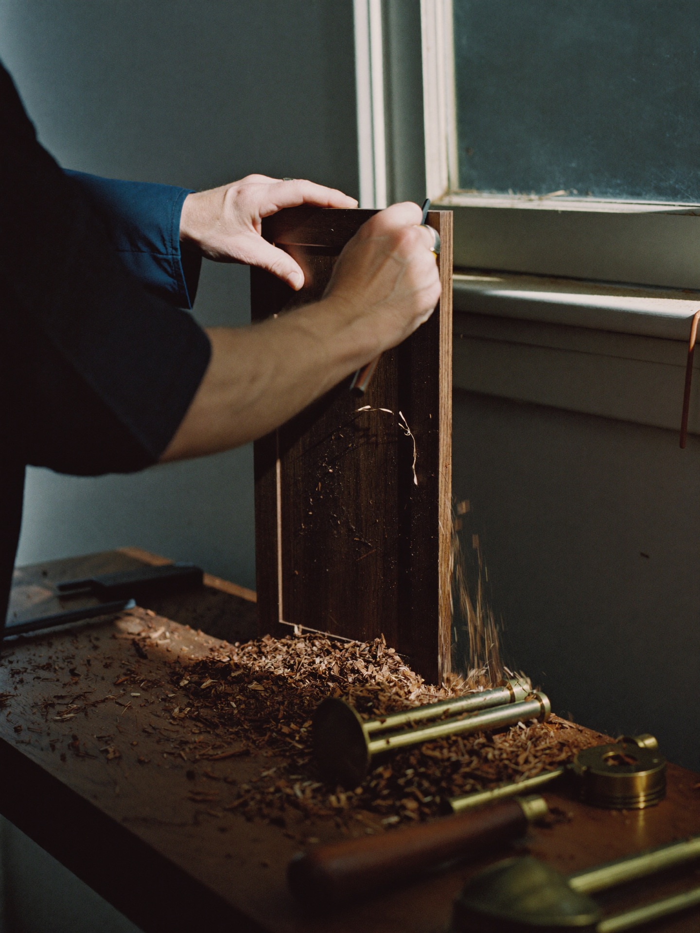 A maker's hands running a hand plane along a length of walnut in the cabinetry shop, curls of shaving on the bench